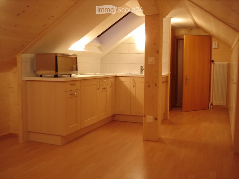 Bright kitchen with wooden cabinets, a microwave, a sink, and a faucet, featuring wooden flooring and a slanted ceiling with skylight windows.