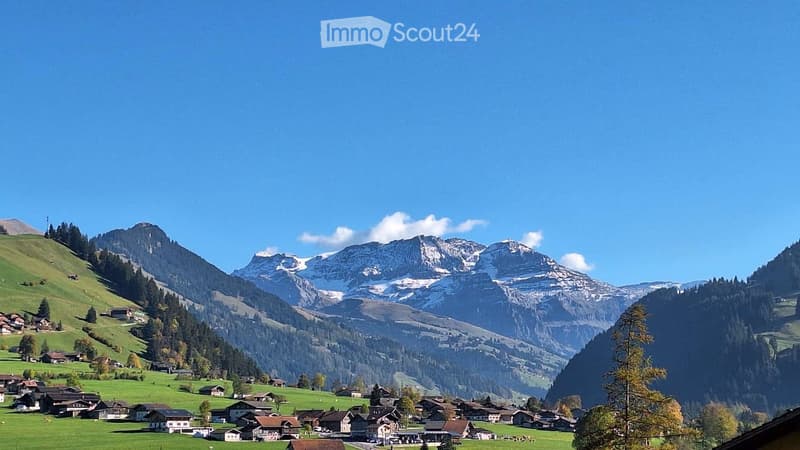 A picturesque alpine village nestled in a lush green valley surrounded by snow-capped mountains under a clear blue sky.