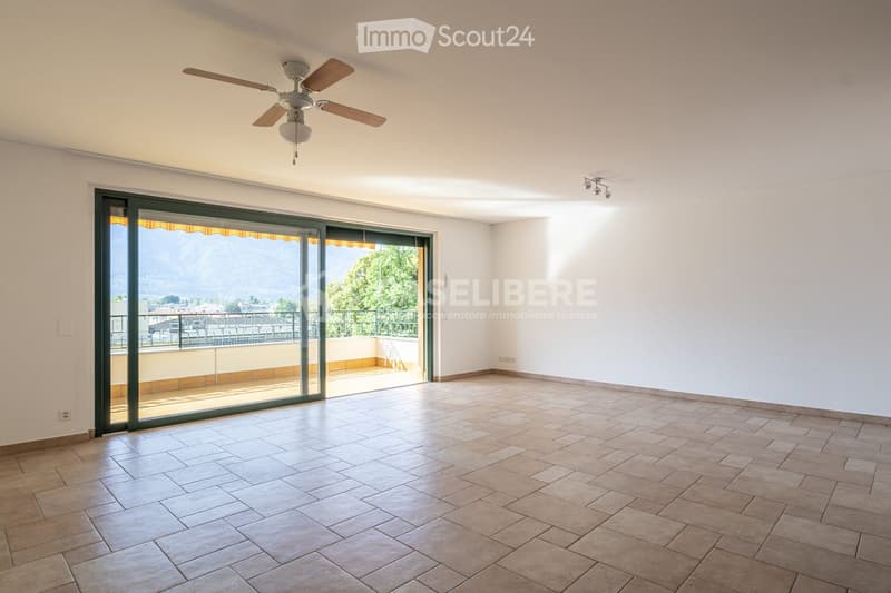 Empty room with tiled floor, white walls, ceiling fan, large sliding glass doors opening to a balcony with a scenic mountain view.