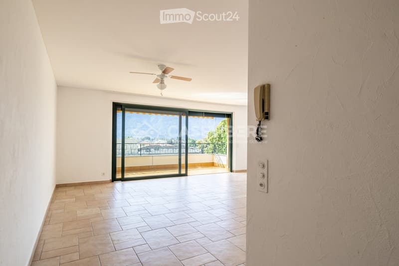 Empty hallway with tiled floor, white walls, ceiling fan, and large sliding glass door leading to a balcony with a scenic view.