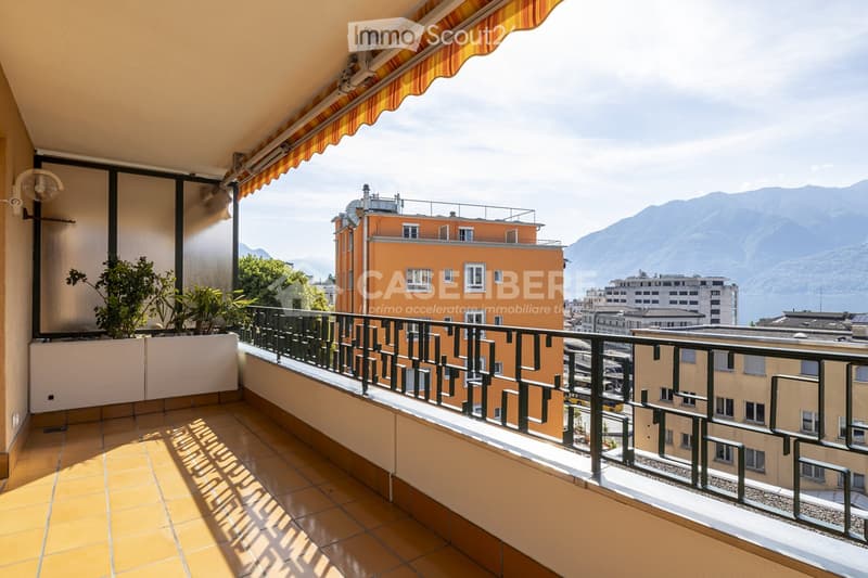 Balcony with tiled floor, metal railing, potted plants, and scenic mountain and lake view.