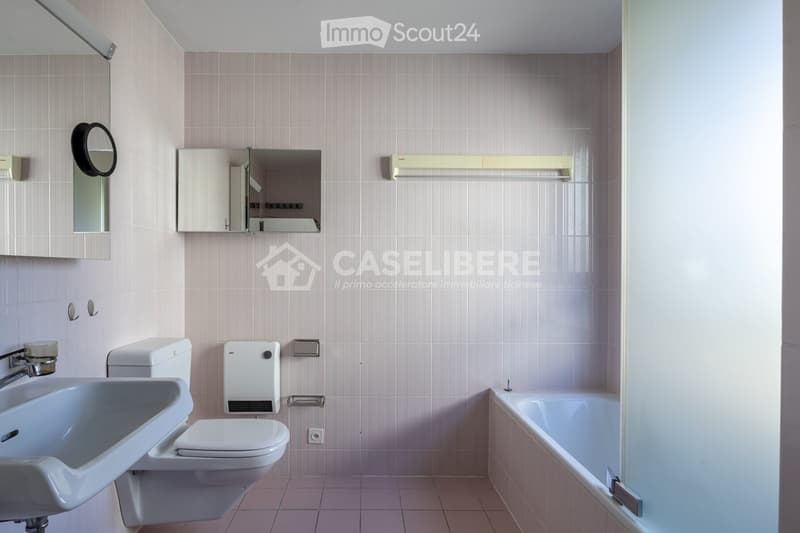 Bathroom with light pink tiles, a white sink, toilet, bathtub, and a mirrored cabinet.