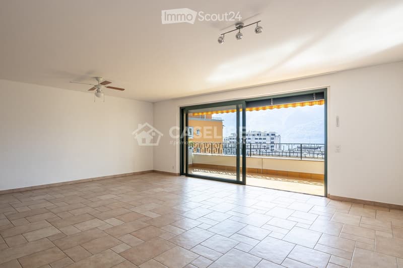 Empty room with tiled floor, white walls, ceiling fan, track lighting, and large sliding glass door leading to a balcony with a view.