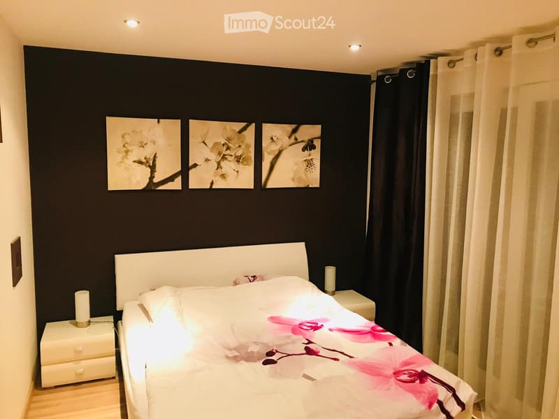 Bedroom with a bed, nightstands, and a wall with three framed pictures. The bed has a white headboard and a floral bedspread. The nightstands have lamps on them. The wall is painted black and has three framed pictures of flowers. The room has a wooden flo