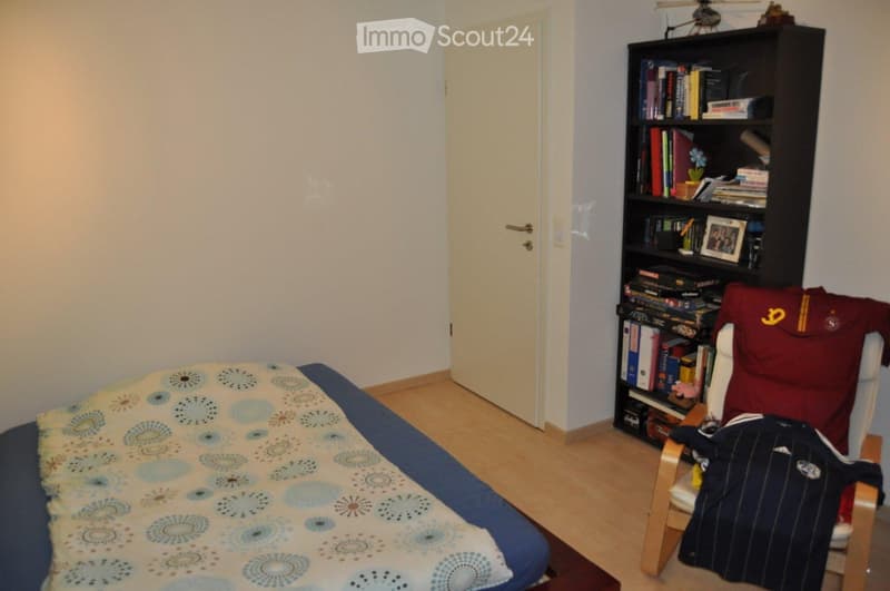 Single bed, bedspread, wooden floor, white door, bookshelf, chair with clothes