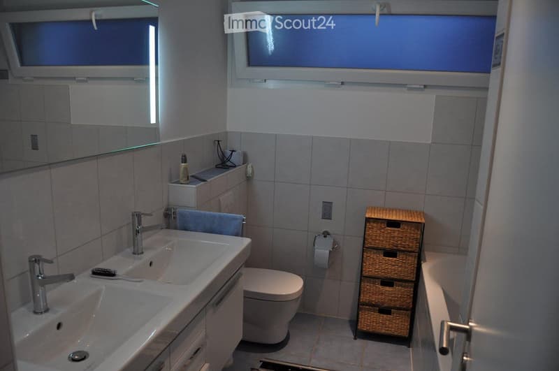 modern bathroom with double sink, toilet, bathtub, and storage shelves
