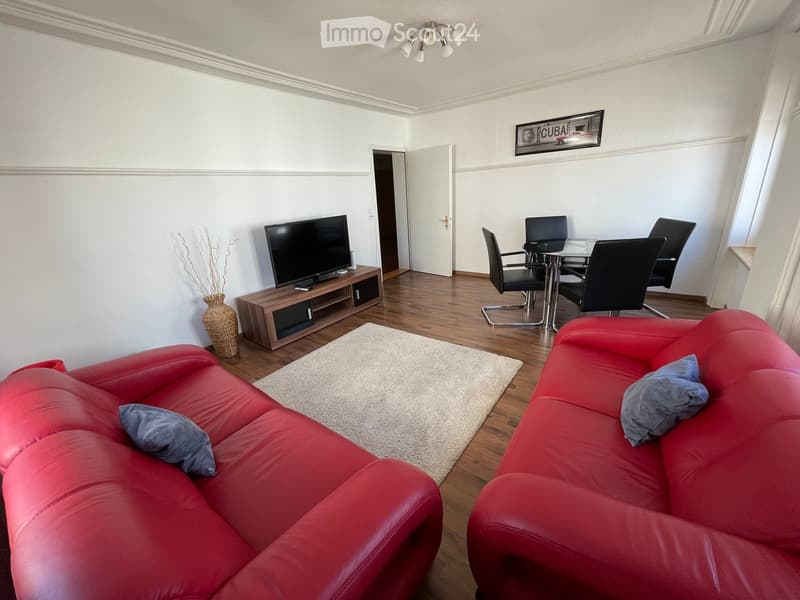Modern living room with red leather sofa, glass dining table, chairs, TV, and decorative vase.