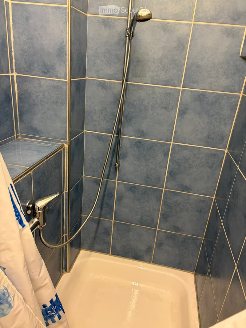 Bathtub with a modern showerhead and faucet, blue tiled walls with gold trim, and a towel hanging on the side.