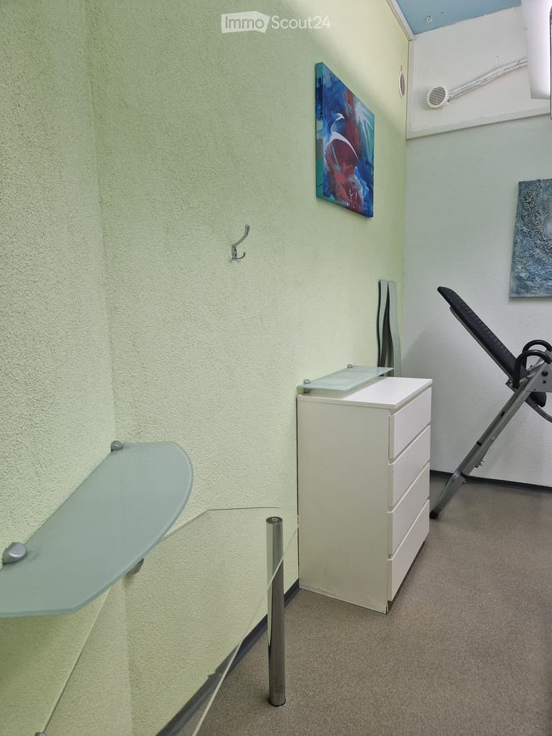 A small, unfurnished room with a white cabinet, a glass table, and an ironing board leaning against the wall.