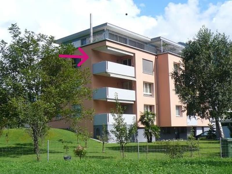 Modern multi-story residential building with balconies, surrounded by greenery and trees.