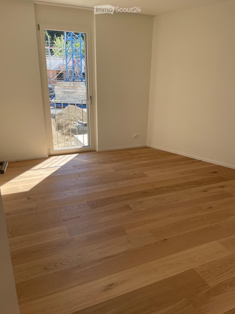 Empty room with light wooden flooring and white walls, featuring a sliding glass door leading outside.