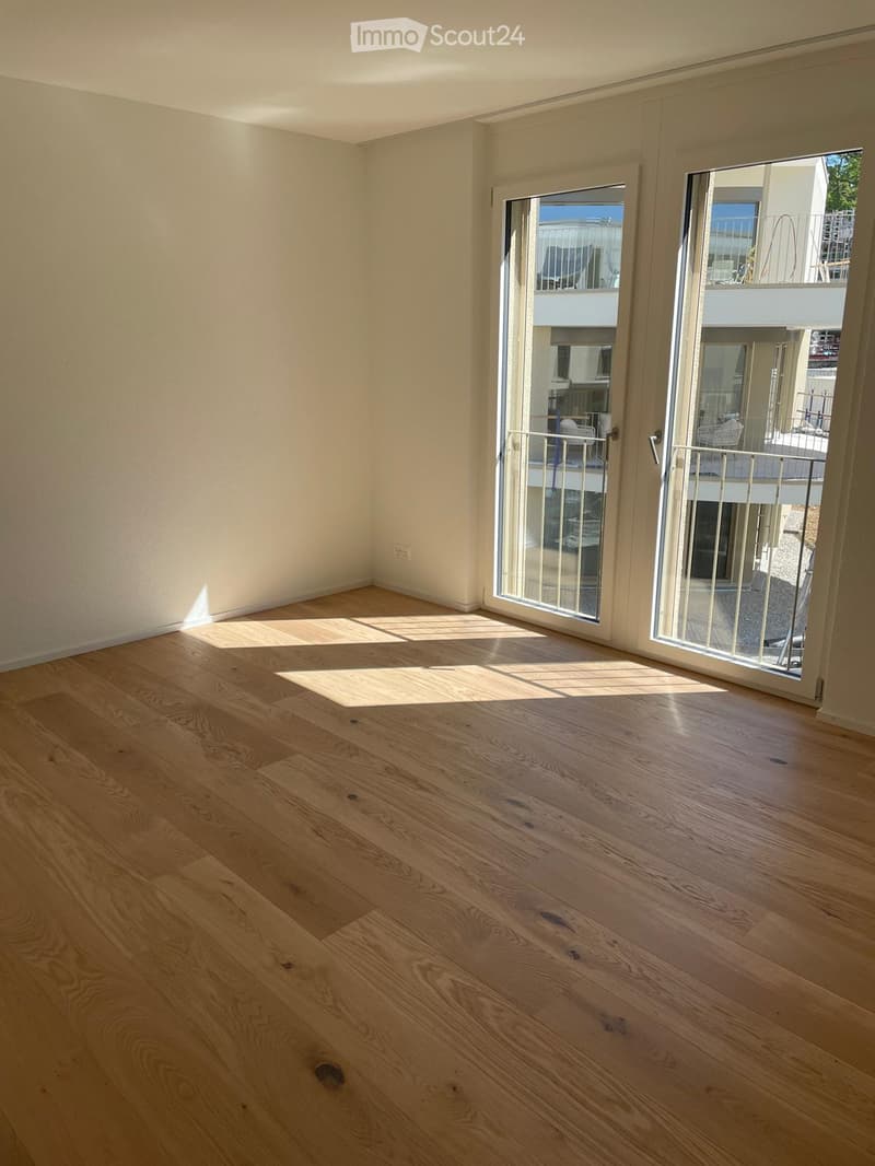 Empty room with light wooden flooring and large sliding glass doors leading to a balcony.