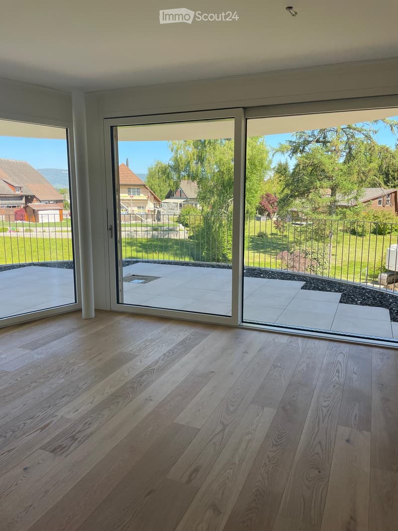 Bright, spacious room with large sliding glass doors opening to a tiled patio and a green, landscaped garden with trees and neighboring houses visible.