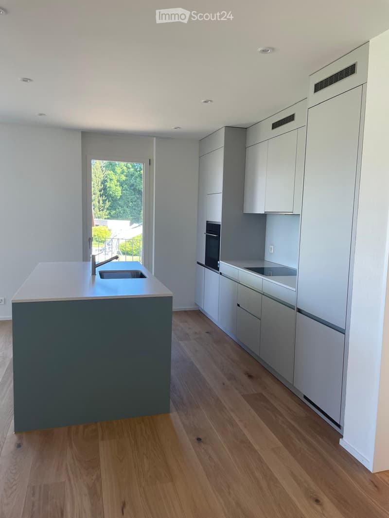 Modern kitchen with white cabinets, a dark grey island, and a wooden floor. Features a sink with a faucet, an oven, and ample cabinet space.