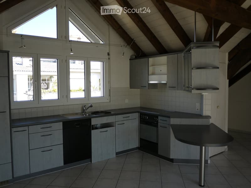Modern kitchen with light grey cabinets, stainless steel appliances, and a central island. Features a sink, dishwasher, stove, and ample windows providing natural light.