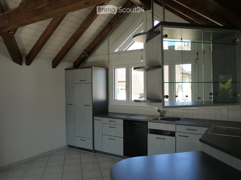 Modern kitchen with grey cabinets, stainless steel sink, dishwasher, and island. Exposed wooden beams on the ceiling and skylights provide natural light.