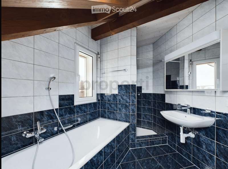 Modern bathroom with white tiles, dark blue lower tiles, a bathtub, a sink, and a mirror above the sink.