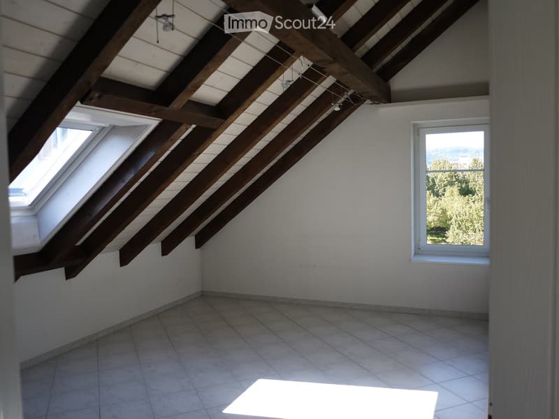 Empty attic room with exposed wooden beams, tiled floor, skylight window, and a large window showing outdoor view.