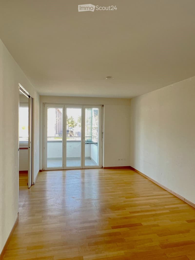 Empty room with wooden flooring, white walls, and large sliding glass doors leading to a balcony.