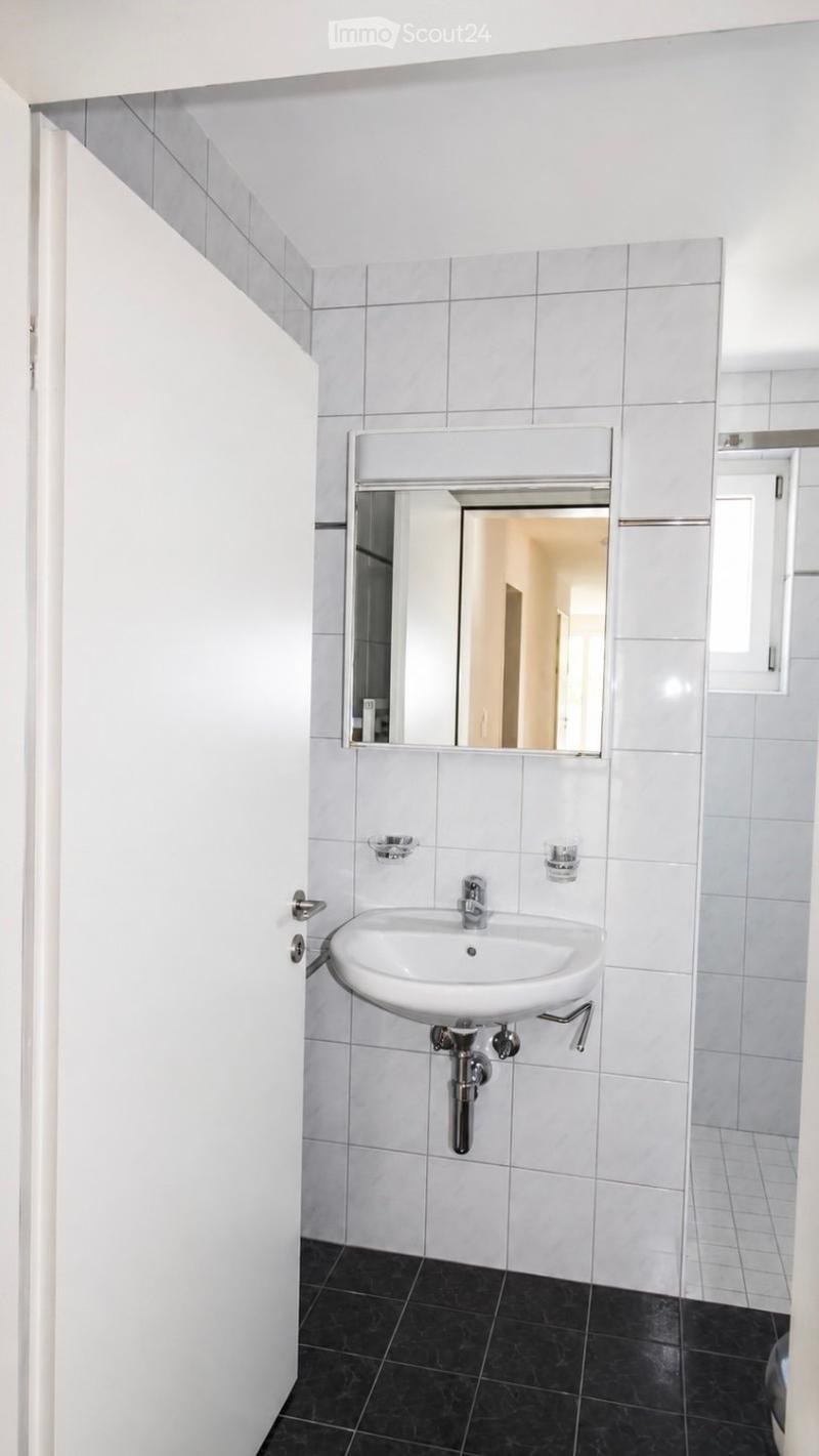 Modern bathroom with white tiled walls, black tiled floor, white sink, and a large mirror above it.