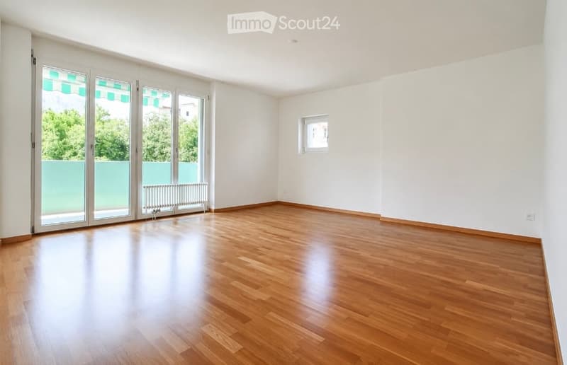 Empty room with wooden flooring, large glass sliding doors leading to a balcony, and white walls.