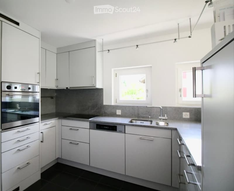 Modern kitchen with white cabinets, stainless steel appliances, and a dark grey backsplash.