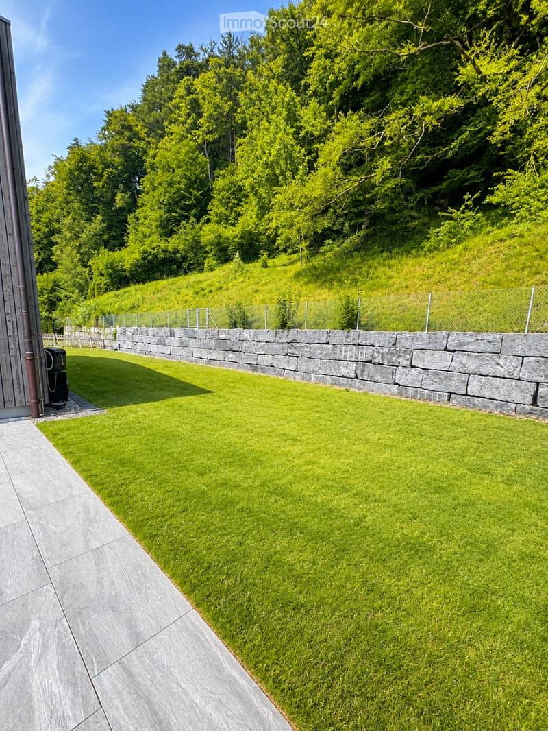 Well-maintained garden with a neatly trimmed lawn, stone wall, and surrounding trees.