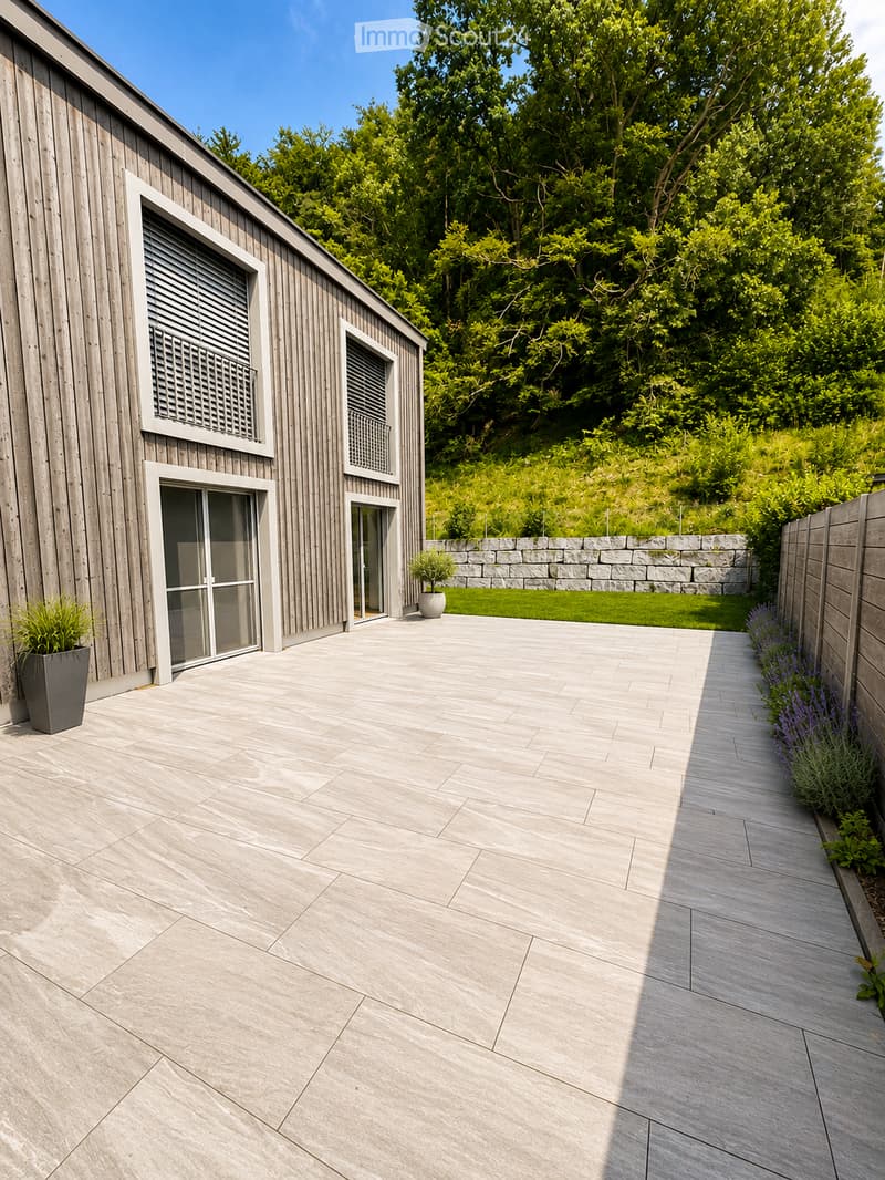 Modern outdoor patio with stone tiles, wooden fence, potted plants, and lush greenery in the background.