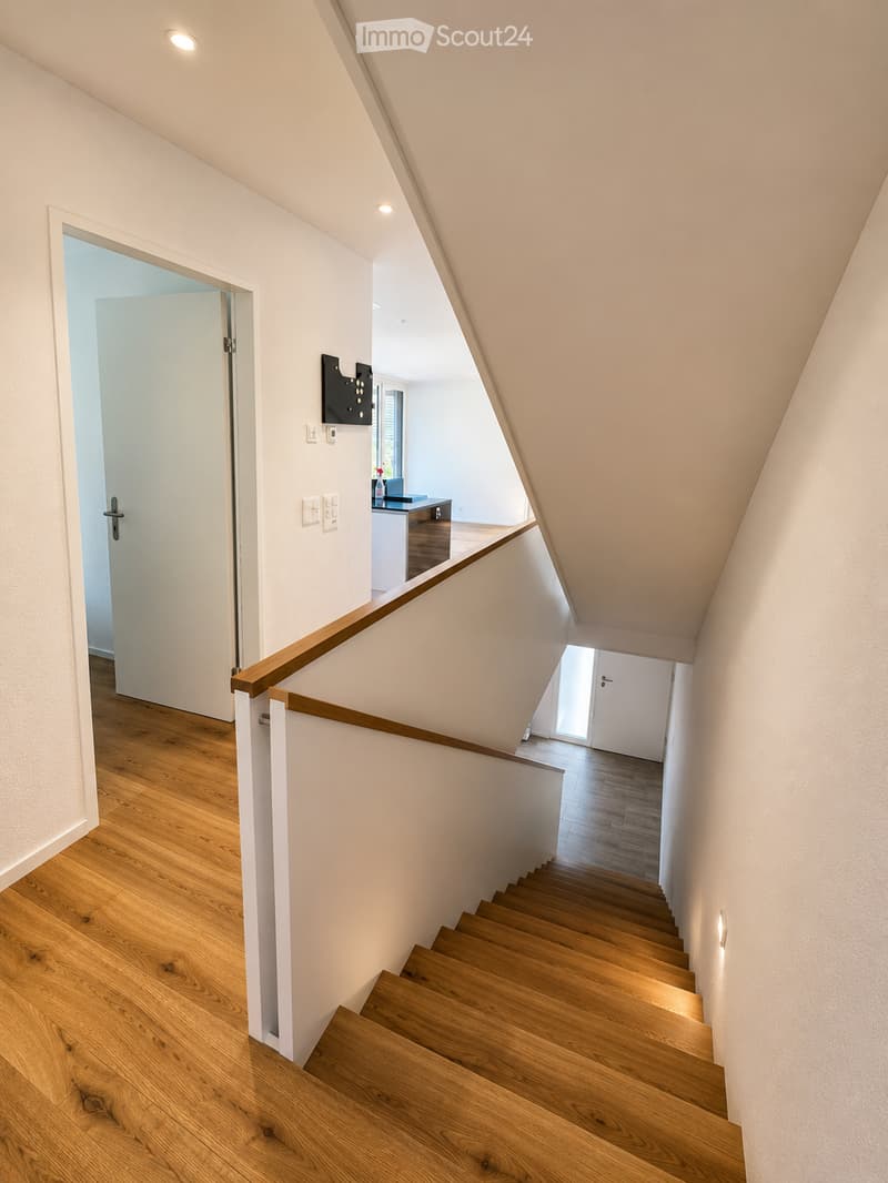 Modern staircase with wooden steps and handrail, white walls, recessed lighting, and open doorways leading to adjacent rooms.