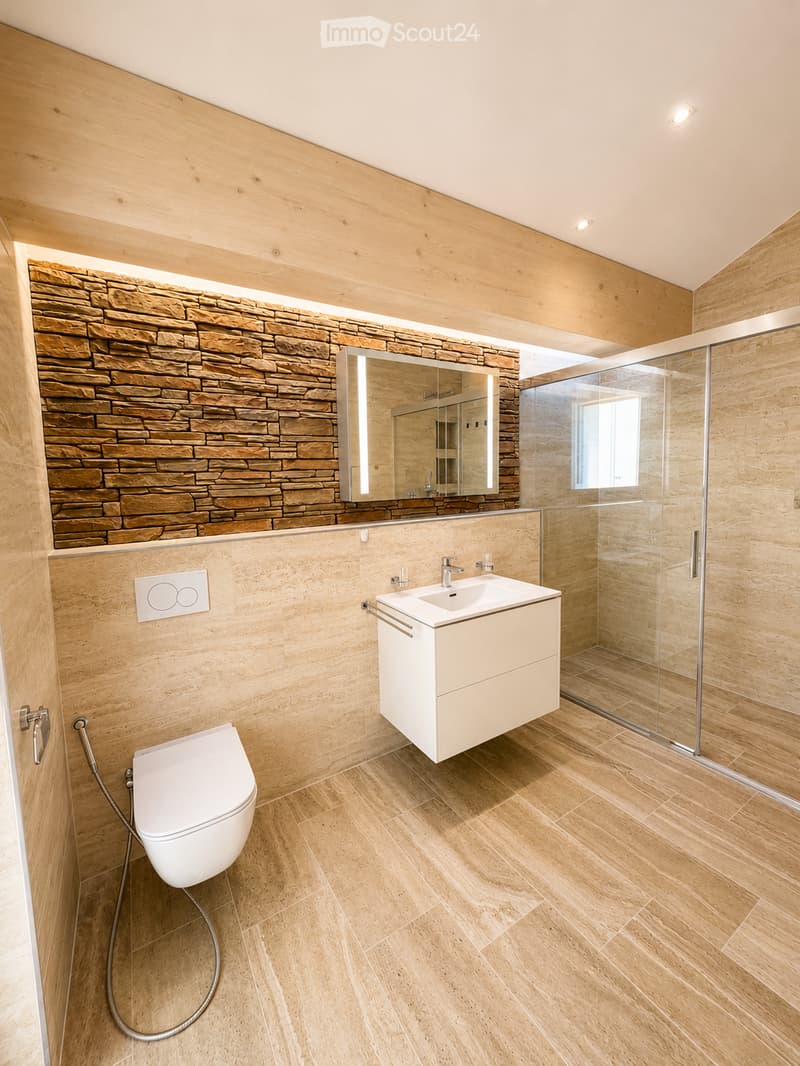 Modern bathroom with wooden walls, stone accent wall, white toilet, sink, and mirrored cabinet.