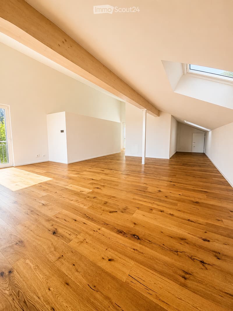 Empty attic room with wooden flooring, white walls, and exposed wooden beams. Features large skylight and sliding glass door leading to a balcony.