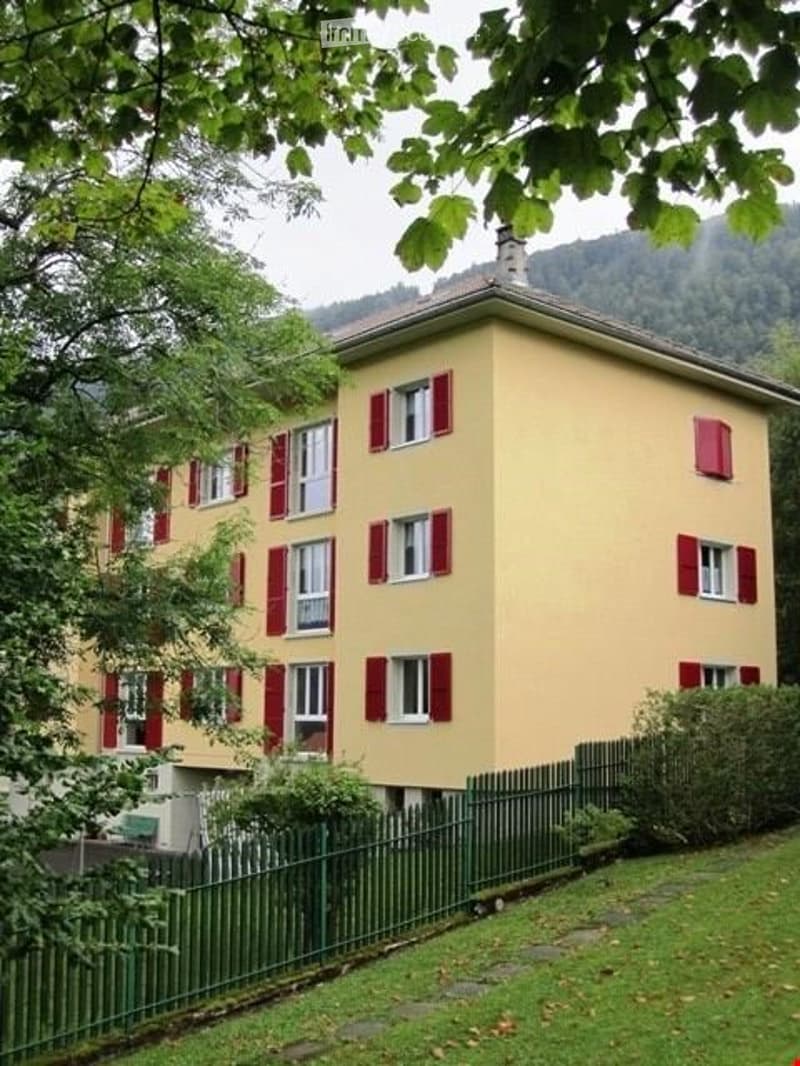 yellow building with red shutters, green fence, mountain view