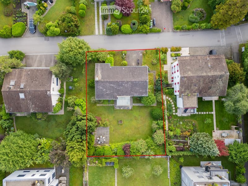 Aerial view of a residential area with multiple houses, well-maintained gardens, and a central patio with a table and chairs.