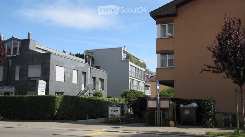Modern multi-story residential buildings with balconies, greenery, and a clear blue sky.