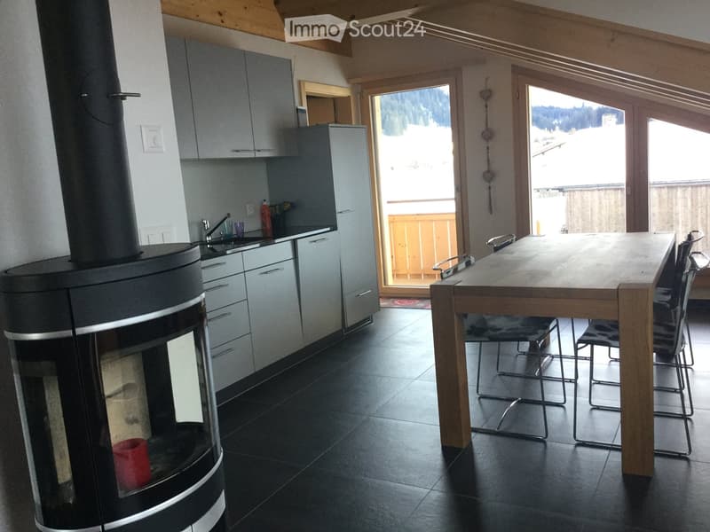 Modern kitchen with a large wooden dining table, chairs, and a view of the mountains through large windows.