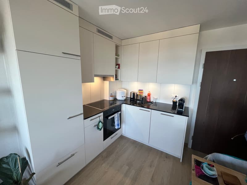 Modern kitchen with white cabinets, stainless steel appliances, and a black countertop. Includes a refrigerator, oven, sink, coffee maker, and microwave.