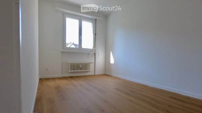 Empty room with wooden flooring, white walls, a window, and a radiator.