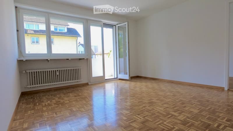 Empty room with wooden parquet flooring, white walls, large windows, and a radiator under one window. No furniture or equipment present.
