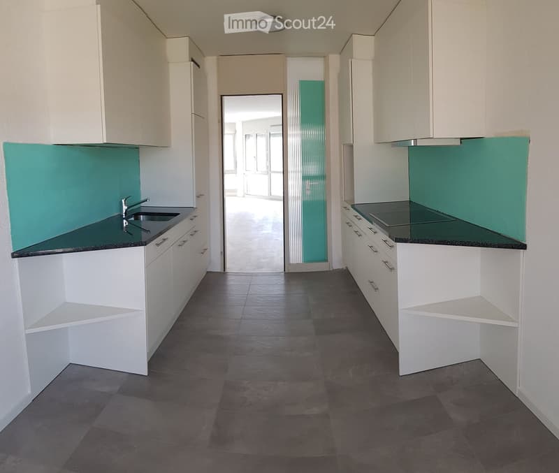 Empty kitchen with white cabinets, dark countertops, and a sink. The space features a tiled floor and an open doorway leading to another room.