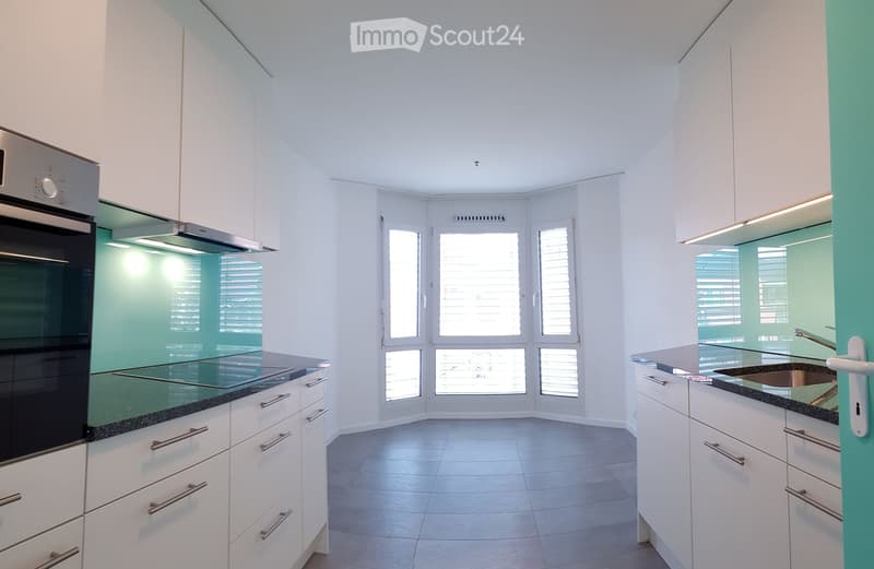 Modern kitchen with white cabinets, stainless steel oven, and a sink, featuring large windows with blinds and a clean, minimalist design.