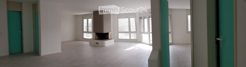 Empty room with wooden flooring, white walls, large windows with blinds, and a fireplace in the center.