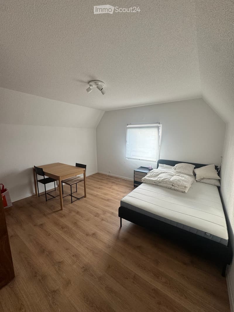 Bedroom with wooden flooring, a bed with white bedding, a nightstand, a small table, and chairs.
