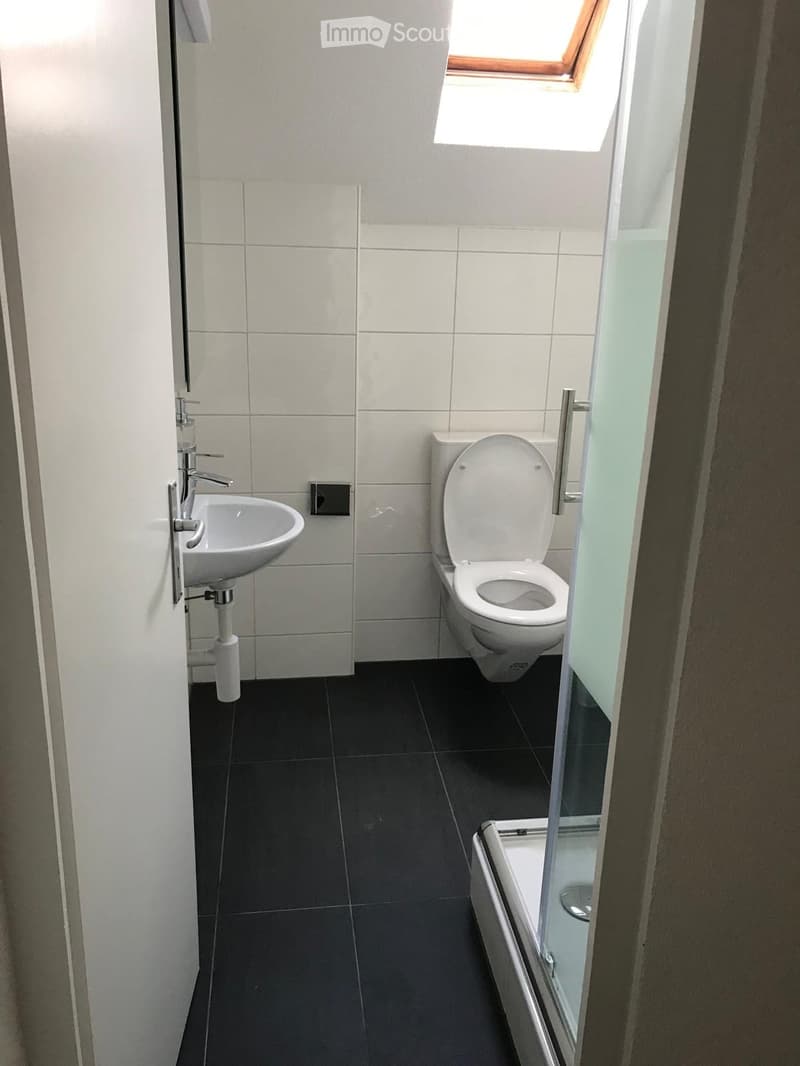 Modern bathroom with white tiles, dark grey floor, sink, toilet, and bathtub with glass enclosure.