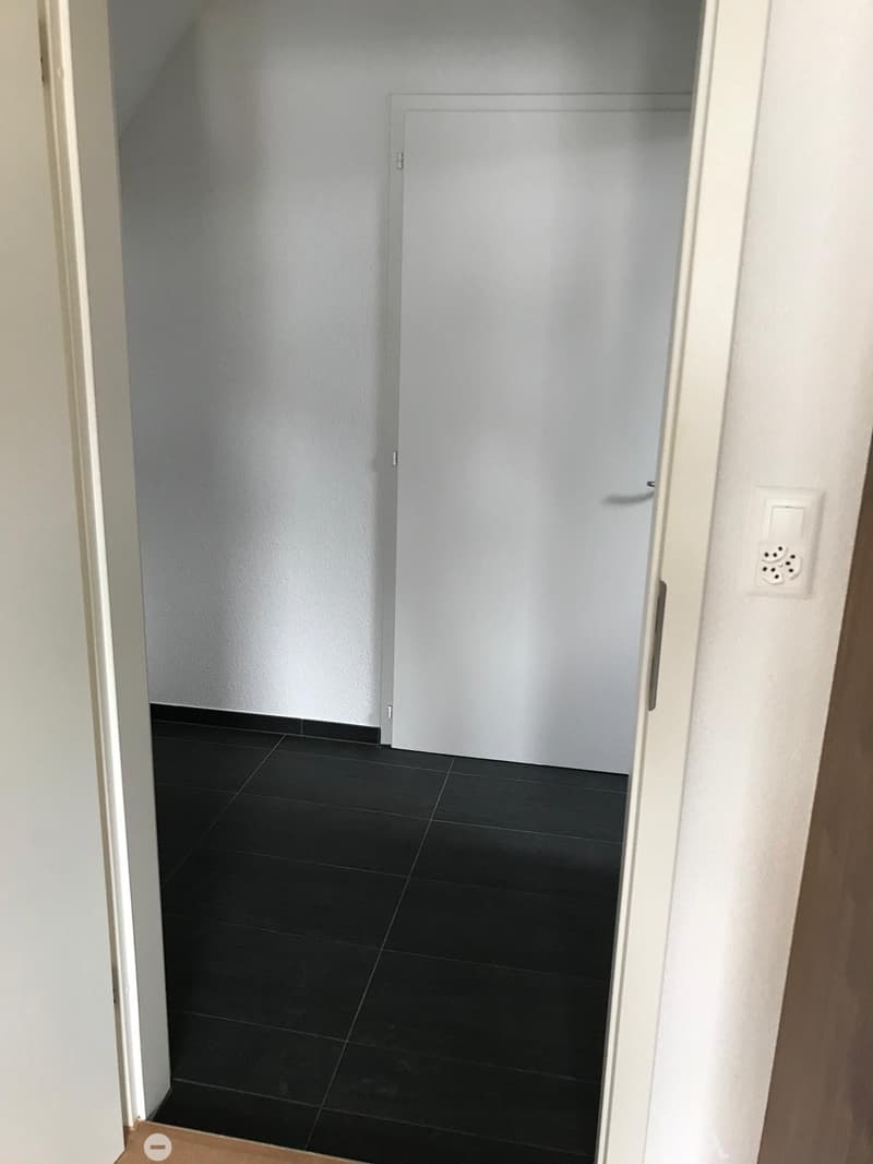 Empty room with black tiled floor and white walls, featuring a closed white door and a visible electrical outlet on the wall.