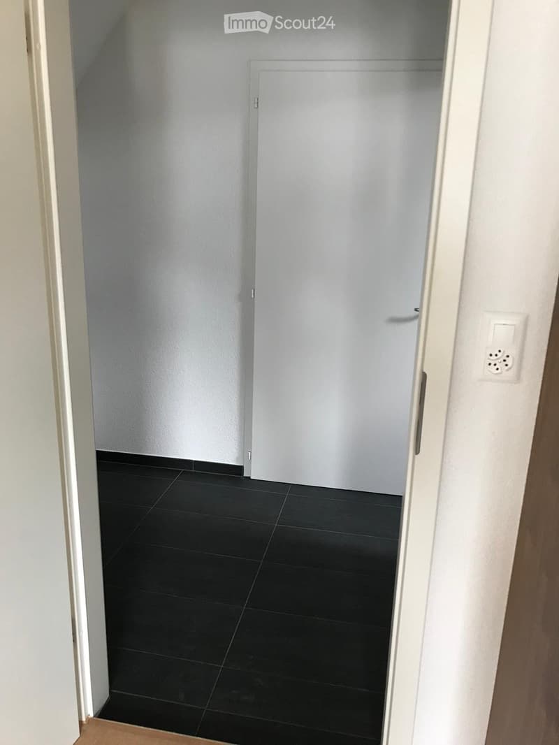 Empty room with black tiled floor and white walls, featuring a closed white door and a visible electrical outlet on the wall.