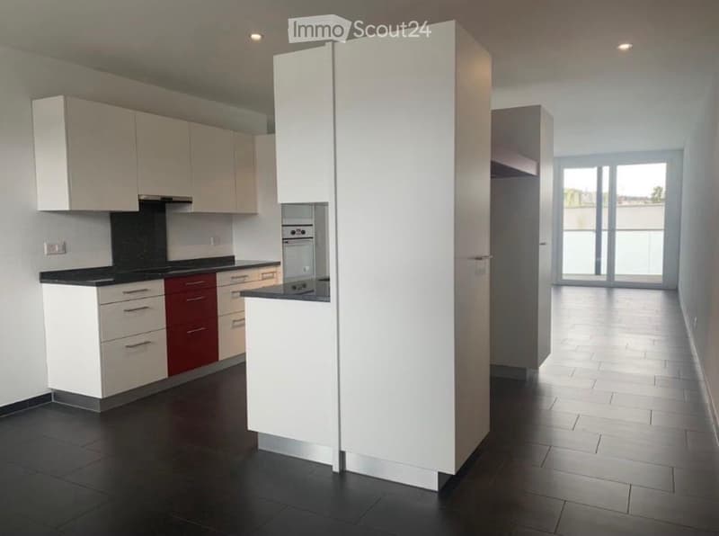 Modern kitchen with white cabinets, black countertop, and stainless steel appliances, including an oven and refrigerator. The space features a large window with a view of the outside area.