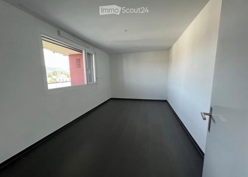 Empty room with white walls, dark tiled floor, and a window with blinds. No furniture or equipment present.
