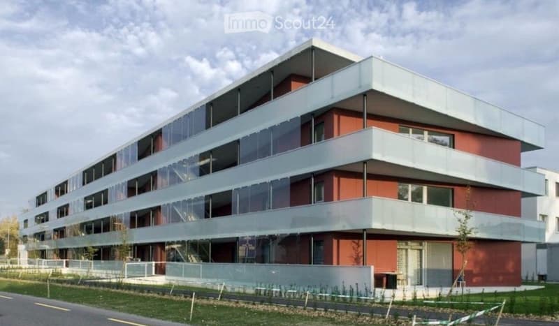 Modern multi-story building with red brick and white accents, large glass windows, and balconies.