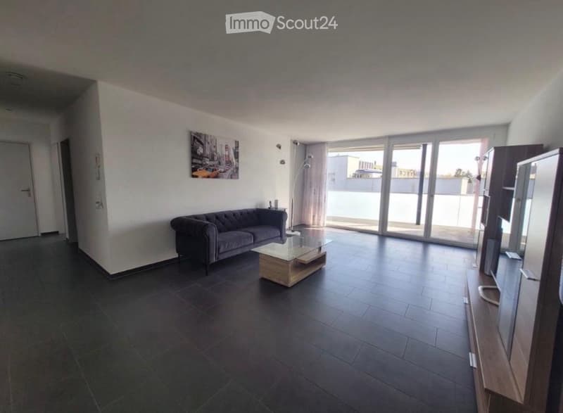 Modern living room with dark tiled flooring, grey sofa, glass coffee table, TV stand, and large sliding glass doors leading to a balcony.