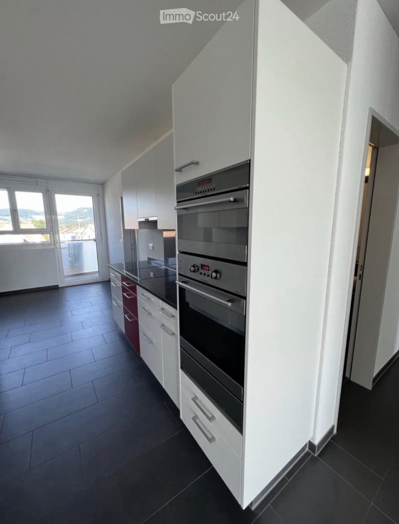 Modern kitchen with white cabinets, stainless steel oven, black countertops, and tiled flooring.